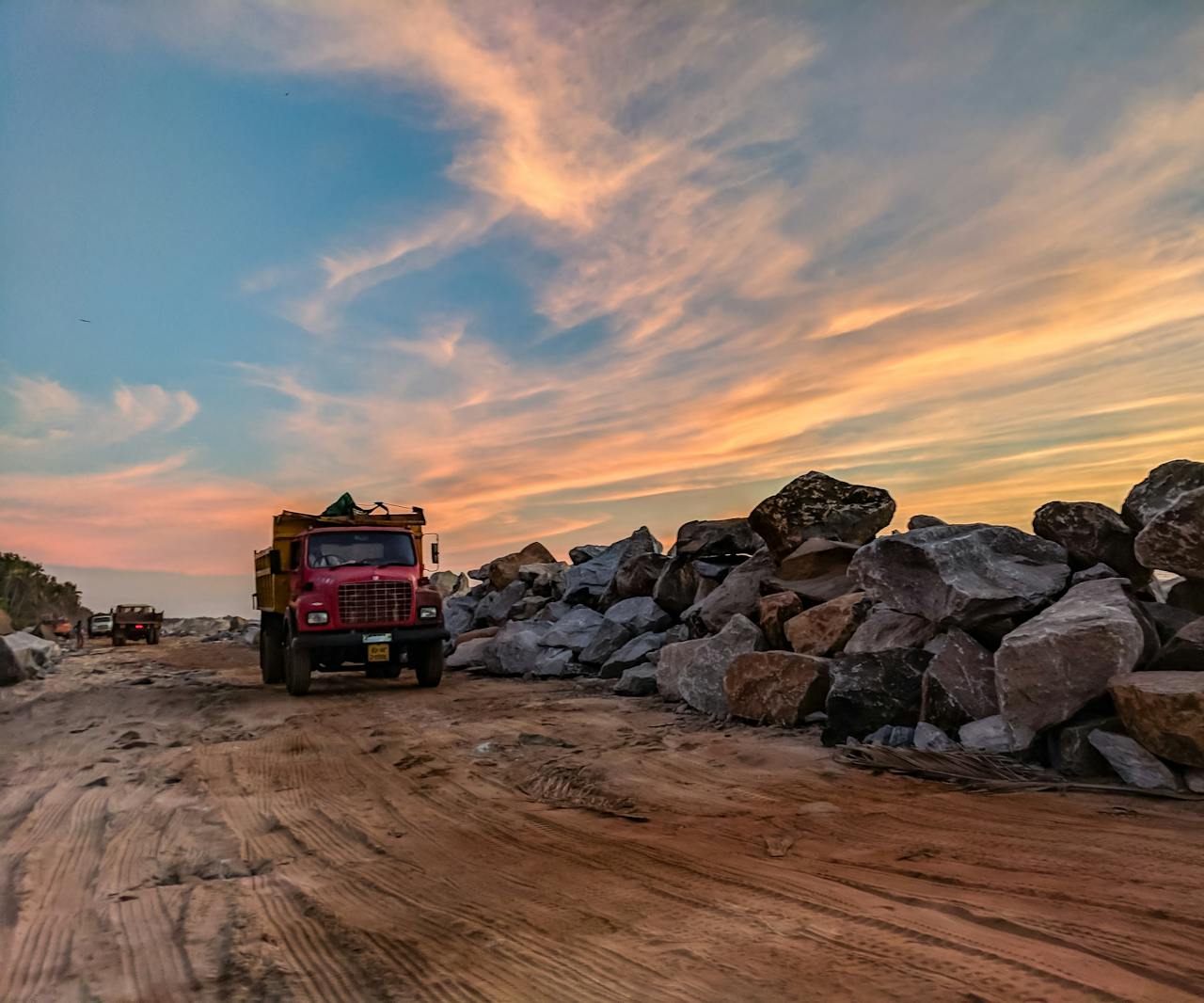Vibrant sunset over trucks and rocks on a busy construction site, highlighting industrial work.